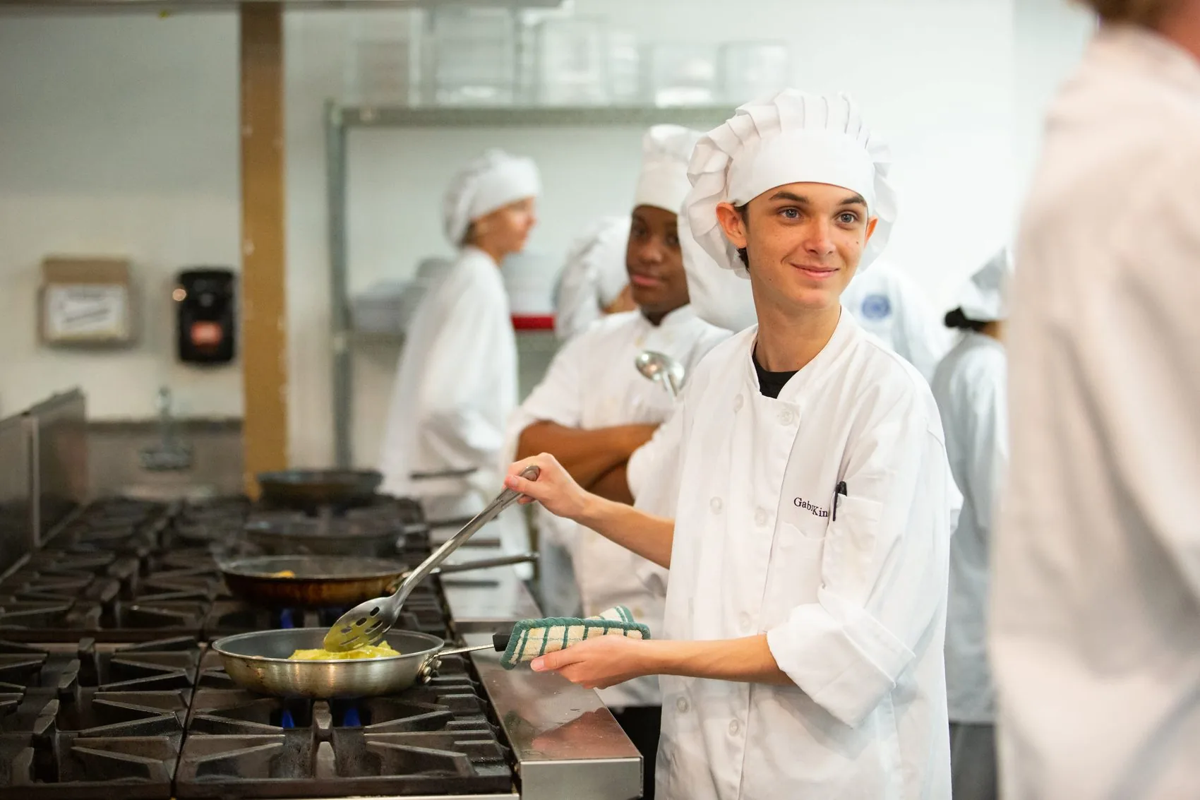 A student in chef whites working at the range in the school kitchen.